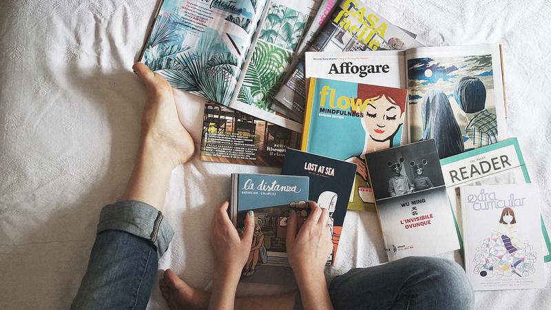 A person sitting on a bed surrounded by books and magazines